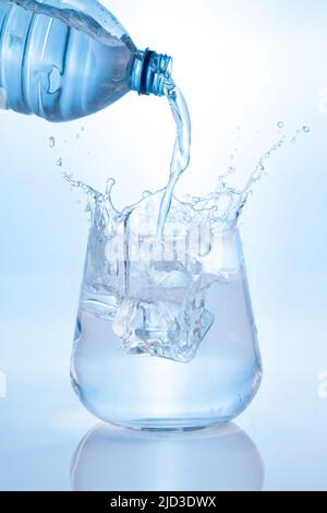 Mineralwasser gießen und aus der Flasche ins Glas auf blauem Hintergrund spritzen. Vertikales Format. Stockfoto