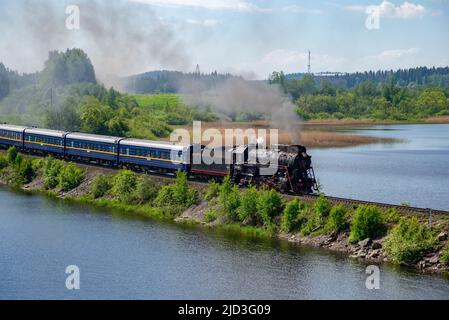 RUSKEALA, RUSSLAND - 11. JUNI 2022: Dampflokomotive mit einem alten Touristenzug 'Ruskeala Express' auf dem Damm des Sees. Karelien Stockfoto