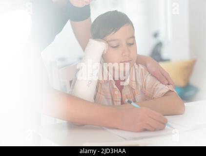 Junge mit gebrochenem Arm in Gips, der Hilfe von einem älteren Bruder für die Hausaufgaben hat. Hochwertige Fotos Stockfoto