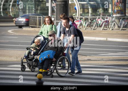 Ein Mann wird gesehen, wie er einen anderen Mann in einem Rollstuhl schiebt und eine Frau, die ein kleines Kind in einem Buggy über eine Straße auf einem Zebrastreifen in Warschau, Polen, schiebt Stockfoto