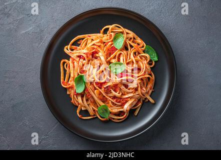 Eine Portion Linguini-Pasta mit Tomaten und Basilikum in Nahaufnahme auf grau-blauem Hintergrund. Stockfoto