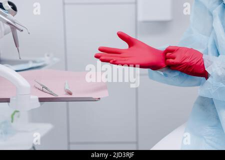 Nahaufnahme der weiblichen zahnärztlichen Frauenhände mit roten sterilisierten Operationshandschuhen in der medizinischen Klinik. Hochwertige Fotos Stockfoto