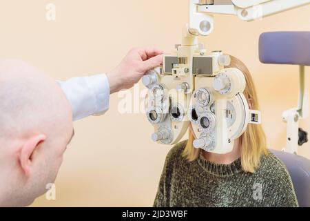 Ein männlicher Augenarzt überprüft das Augenlicht eines Mädchens mit einem Phoropter. Sehbehandlung. Stockfoto