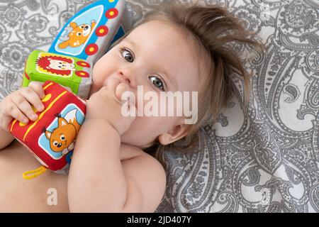Ein Baby mit bunten Würfeln in den Händen spielt auf dem Bett. Babyentwicklungskonzept, Kleinkind erholsamer Schlaf, Zahnen, Koliken. Blick von oben. Stockfoto