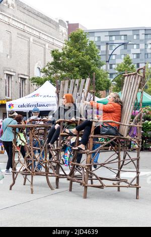 Everett, WA - USA -06-10-2022: Zwei Frauen sitzen auf übergroßen Holzstühlen beim Sorticulture Festival in der Innenstadt Stockfoto