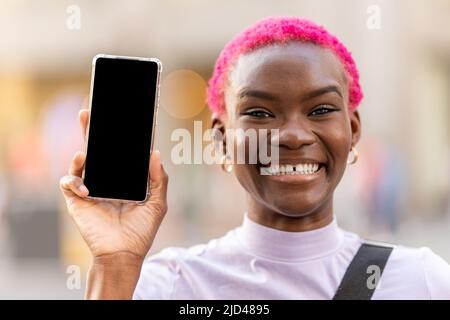 Afro-Frau mit toothy Lächeln zeigt den Bildschirm von Handy Stockfoto
