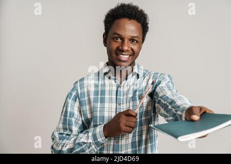 Schwarzer unrasierer Mann im karierten Hemd, der mit einem Übungsbuch auf weißem Hintergrund posiert Stockfoto