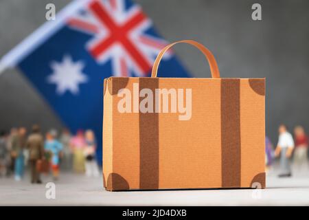 Pappkoffer, Plastikspielzeug Menschen und eine Flagge auf abstraktem Hintergrund, ein Konzept zum Thema Umzug oder Einwanderung nach Australien Stockfoto