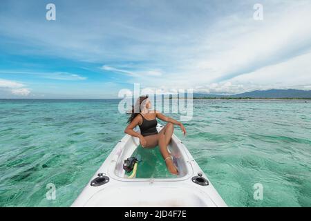 Junge Indonesierin im schwarzen Badeanzug, die in einem weißen Kajak mit türkisfarbenem Wasser sitzt Stockfoto