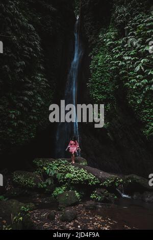 Junge Indonesierin, die auf Felsen am Leke Leke Wasserfall im Dschungel von Ubud Bali Indonesia steht Stockfoto