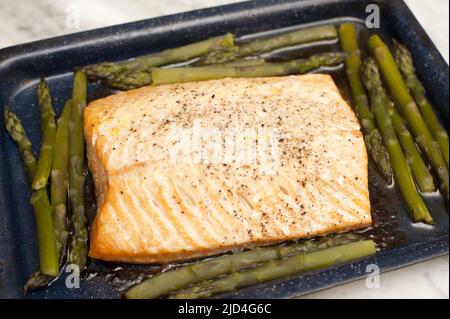 Eine Portion köstlicher, im Gourmet-Ofen gebackener Lachs und grüner Spargelspieße in einem Backblech direkt aus dem Ofen für eine gesunde Meeresfrüchteküche Stockfoto