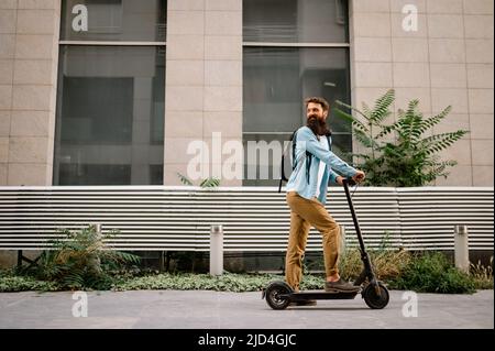 Junge Hipster Mann fahren Elektroroller nach der Arbeit. Ökologisches Transportkonzept. Stockfoto