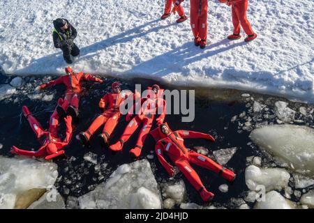 Rovaniemi, Finnland - 21.. März 2022: Eine Gruppe von Touristen schwimmt im gefrorenen Wasser der auftauenden ostsee mit Isolieranzügen. Stockfoto