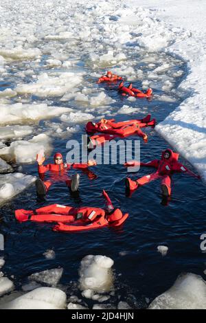 Rovaniemi, Finnland - 21.. März 2022: Eine Gruppe von Touristen schwimmt im gefrorenen Wasser der auftauenden ostsee mit Isolieranzügen. Stockfoto