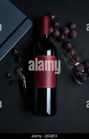 Weinflasche mit Glas, Trauben, Flaschenöffner und Notizbuch, dunkler Hintergrund Stockfoto