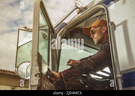 Caucasian Trucker bei seinem 40s stolz sitzen in seinem großen Semi-Truck Blick durch das Seitenfenster bereit, den Weg zu gehen. Stockfoto