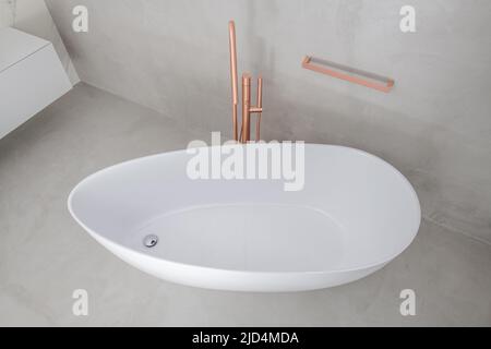 Minimalistische, freistehende weiße Badewanne mit goldener Badewannenfüller in frisch renovierten Badezimmern in modernem Stil, die in hellgrau und beigen Farben gehalten sind. Lux Stockfoto