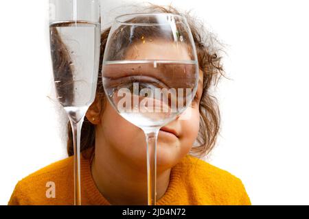 Mode Kind Porträt, Auge schaut durch das Glas Wasser. Objektverzerrung, optisches Illusionskonzept. Minimalistische zeitgenössische Kunst. Hohe Qualität Stockfoto