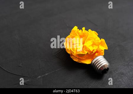 Glühbirnenform aus einer zerknitterten Papierkugel auf schwarzem Hintergrund. Kreatives Konzept zur Ideenentwicklung. Stockfoto