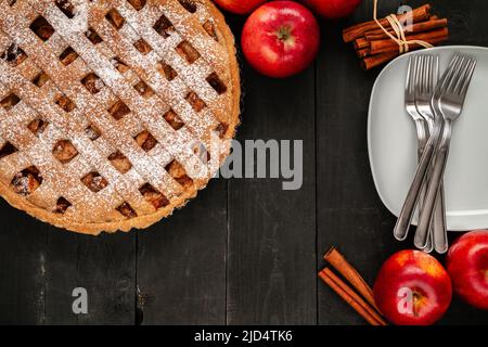 Köstlicher hausgemachter Apfelkuchen, mit Äpfeln, Zimtstangen und weißem Teller mit Besteck. Thanksgiving Dinner flach legen Zusammensetzung auf einem Holztisch. Stockfoto