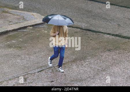 Ein Mann geht bei Regen mit Sonnenschirmen die Straße hinunter. Hochwertige Fotos Stockfoto