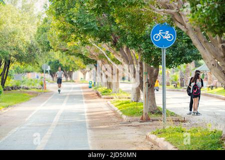 19. Mai 2022, Antalya, Türkei: Radfahrer und Roller fahren auf einem Radweg in einem Park mit bemaltem Gehweg und Straßenschildern. Fußgänger gehen in der Nähe Stockfoto
