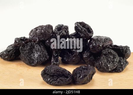 Getrocknete Pflaumen auf Holzplatte und hellem Hintergrund. Nahaufnahme. Stockfoto