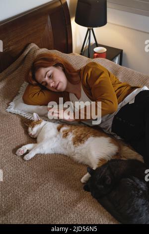 Frau mittleren Alters hält niedlichen Ingwer Katze. Frau umarmt ihre schöne kurze Haare Kitty im Schlafzimmer am Abend. Speicherplatz kopieren. Entzückendes Haustier Stockfoto