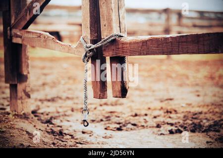 Der Boden eines alten hölzernen Paddock-Tores auf einer Farm, geschlossen an einem Bleiseil, verknotet an einem bewölkten Tag. Ein leeres Paddock für Hausrinder. Ländliche Gegend. Stockfoto