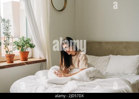 Eine schöne Brünette junge Frau, die nach dem Aufwachen am Morgen ihr Telefon überprüft Stockfoto