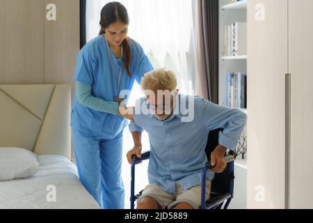 Asiatische lächelnde Krankenschwester helfen älteren Mann aus dem Bett Krankenpflege unterstützen Patienten, während aus dem Bett und bewegen sich in den Rollstuhl zu Hause helfen h Stockfoto