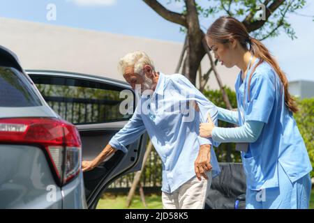 Junge asiatische Frau Krankenschwester Pflegeperson hilft behinderten älteren Menschen in Auto vor der Heimat. Stockfoto