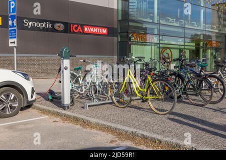 Parkplatz für Fahrräder und Blick auf das angeschlossene Ladekabel zum Auto von der Ladestation für Elektrofahrzeuge des städtischen Einkaufszentrums von Uppsale. Swe Stockfoto
