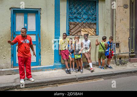 Mann in roter Kleidung mit einer Gruppe von Kindern in einer Straße in der Altstadt von Havanna, Kuba Stockfoto