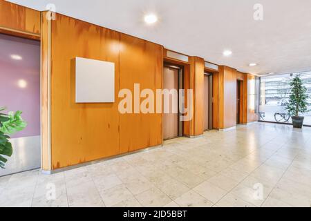 Glänzender Aufzug mit geöffneter Tür in der beleuchteten Halle eines modernen Apartmentgebäudes mit Fliesenboden Stockfoto