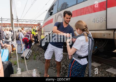 Hertogenbosch, Niederlande. 18 Juni 2022. Eine alleinreisende Mutter mit einem kleinen Baby wird von einem anderen Reisenden unterstützt, während Passagiere des kaputten ICE-Zuges (ICE 153) zwischen den Gleisen auf den Austausch des Transports warten. Kredit: Steppeland/Alamy Live Nachrichten. Stockfoto