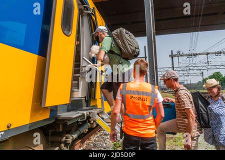 Hertogenbosch, Niederlande. 18 Juni 2022. Der Passagier, der einen Rucksack und einen Hund trägt, steigt mit Unterstützung von Pro Rail-Mitarbeitern über eine befestigte Leiter in den NS-Ersatzzug ein. Kredit: Steppeland/Alamy Live Nachrichten. Stockfoto