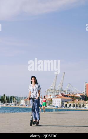 Glücklich Brünette asiatische Frau sitzen, zu Fuß in der Stadt Straße. Park. Lachend an einem sonnigen Sommertag. Spaß haben. Lifestyle Stockfoto