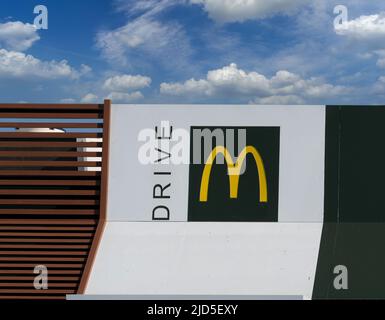 Savigliano, Italien - 16. Juni 2022: McDrive-Schild am neuen McDonald's ristorante am blauen Himmel bewölkt. Die McDonald's Corporation ist die größte Kette der Welt Stockfoto