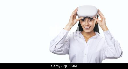 Virtual-Reality-Konzept: Lächelte junge Frau in hellem Hemd mit VR-Brille auf dem Kopf isoliert auf weißem Hintergrund mit Platz für Ihr Logo oder Text, Stockfoto