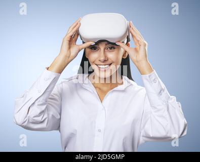 Virtual-Reality-Konzept: Lächelte junge Frau in hellem Hemd mit VR-Brille auf dem Kopf auf hellblauem Hintergrund, Nahaufnahme Stockfoto