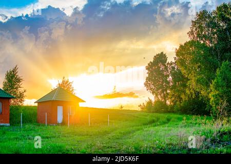 Abendlandschaft, Blick auf einen leuchtend orangefarbenen Sonnenuntergang mit langen Strahlen gegen einen schönen Himmel Stockfoto