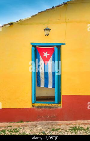 Kubanische Flagge, die in einem blauen Türrahmen eines gelben Hauses in Trinidad, Kuba, hängt Stockfoto