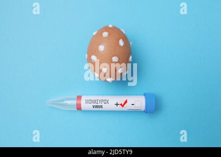 Flatlay mit Monkeypox-Reagenzglas und Ei mit Monkeypox-Symptomen auf blauem Hintergrund. Stockfoto