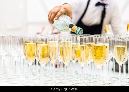 Der Barkeeper gießt Champagner in Gläser. An der Bar gab es ein Glas Champagner. Viele alkoholische Getränke. Stockfoto