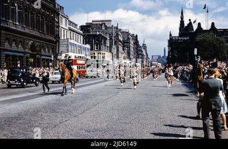 Historisches Foto einer Menge, die eine schottische Pfeifenkapelle beobachtete, die Dudelsäcke spielte, begleitet von einem berittenen Polizisten in einer Parade mit alten Autos und Bussen und einem Blick entlang der Princes Street zum National Monument auf Calton Hill, Edinburgh, Schottland, Großbritannien Ende 1950s Stockfoto