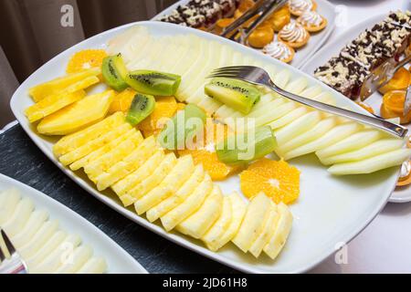 Teller mit geschnittenen Früchten: Ananasscheiben, Kiwi, Orange. Catering auf einem Buffettisch. Stockfoto