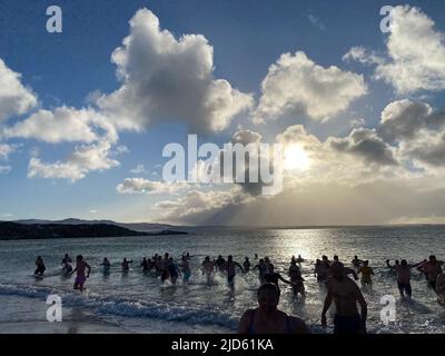 Stanley, Großbritannien. 18.. Juni 2022. Die Teilnehmer des traditionellen Winterschwimmes tauchen aus dem Wasser auf. Dutzende trotzten dem eiskalten Wetter auf den Falklandinseln und sprangen zum Winterschwimmen in den Südatlantik. Quelle: Benedikt von Imhoff/dpa/Alamy Live News Stockfoto