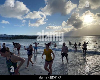 Stanley, Großbritannien. 18.. Juni 2022. Die Teilnehmer des traditionellen Winterschwimmes tauchen aus dem Wasser auf. Dutzende trotzten dem eiskalten Wetter auf den Falklandinseln und sprangen zum Winterschwimmen in den Südatlantik. Quelle: Benedikt von Imhoff/dpa/Alamy Live News Stockfoto