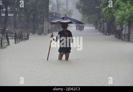 Guwahati, Indien. 18.. Juni 2022. Ein alter Mann geht in einem Dorf im Nalbari-Distrikt von Assam Indien mit einem zerbrochenen Regenschirm auf der überfluteten Straße. (Bild: © Dasarath Deka/ZUMA Press Wire) Stockfoto